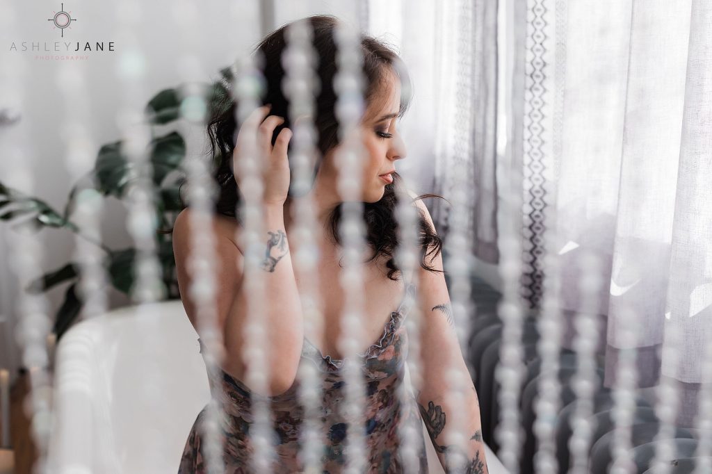 Photos of boudoir model in floral lingerie kneeling in clawfoot tub behind bead curtain.