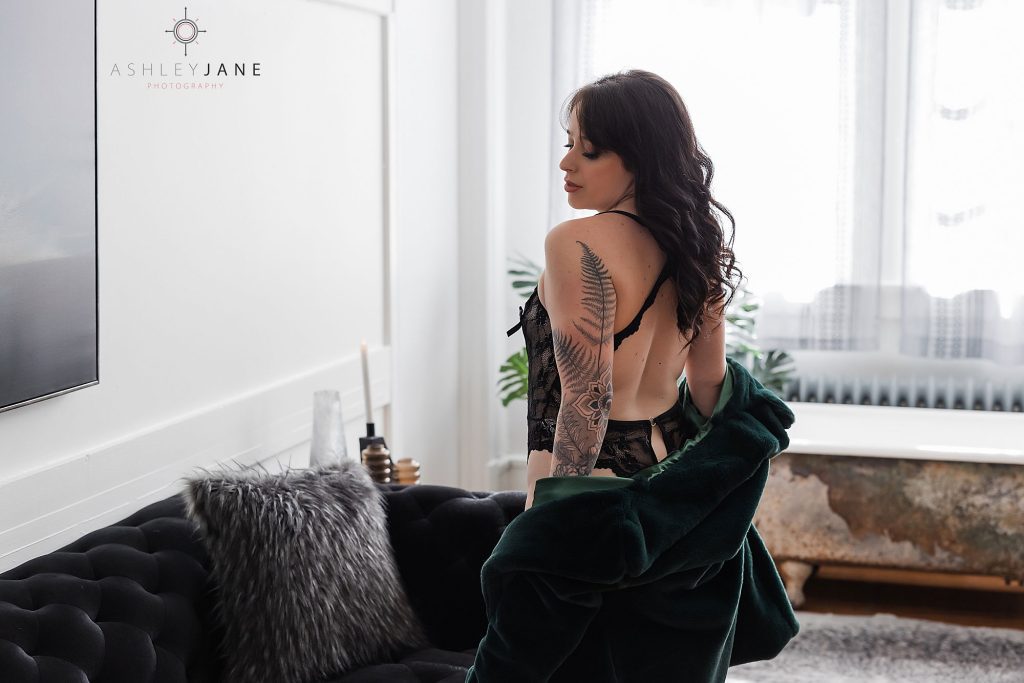 Boudoir model wearing black lingerie removing her green fur coat.