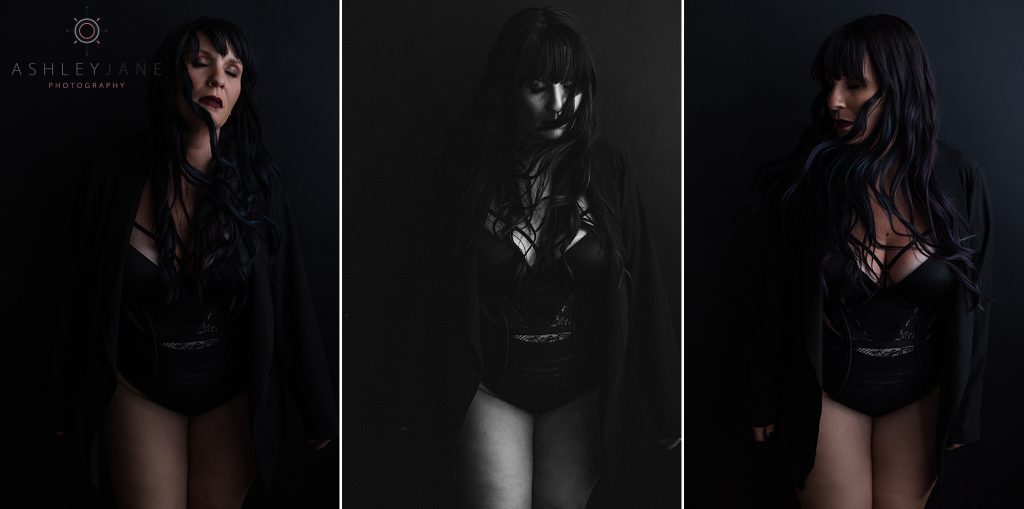 Boudoir model wearing lacy black lingerie under a black jacket standing against a black background.